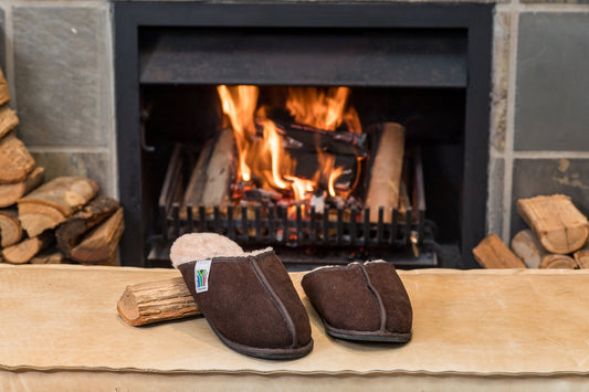 Oskava brown sheepskin slip-ons, one propped on a log by the fire
